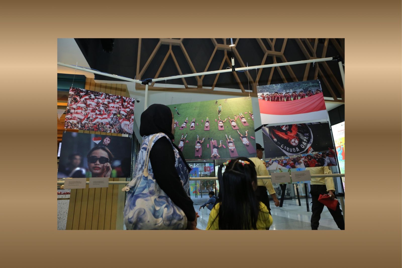 Seorang ibu dan anaknya tampak serius melihat foto dalam Pameran Foto 90’ & Beyond di Mal Sarinah, Jakarta. (Foto: Dok. PFIJ dan PSSI Pers/Grafis: Skor.id)