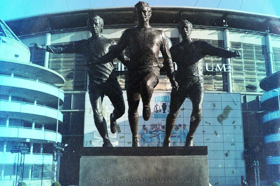 Patung trio pemain legendaris Manchester City: Collin Bell, Francis Lee, dan Mike Summerbee, berdiri megah di Stadion Etihad (Jovi Arnanda/Skor.id).