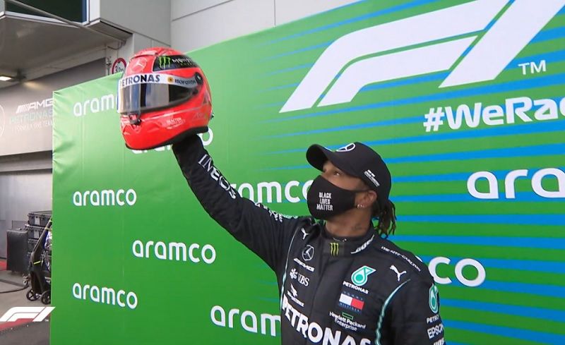 Pembalap Mercedes-AMG Petronas, Lewis Hamilton, mengangkat helm replika milik Michael Schumacher yang diberikan Mick Schumacher sesaat setelah memenangi F1 GP Eifel 2020, Minggu (11/10/2020).