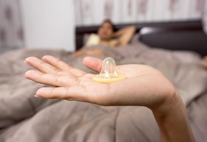 Ilustrasi seorang wanita memperlihatkan sebuah kondom ke arah pasangan. 