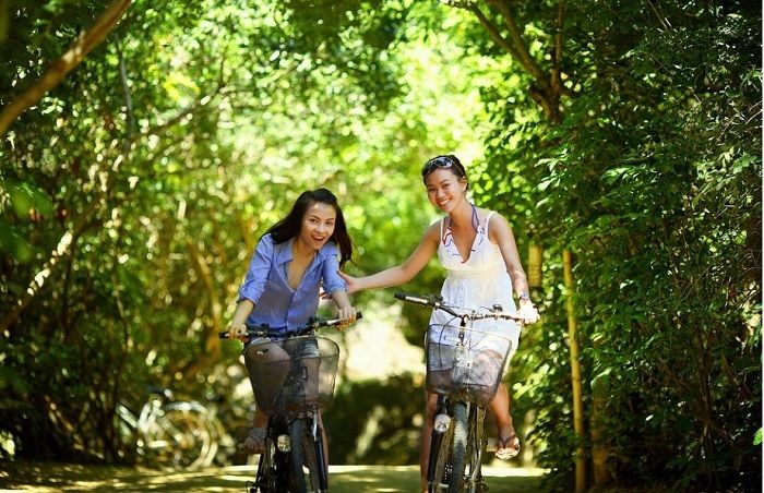 Ilustrasi dua wanita sedang bersepeda dengan senyum lebar, salah satu tanda mereka menjalankan hidup yang sehat.