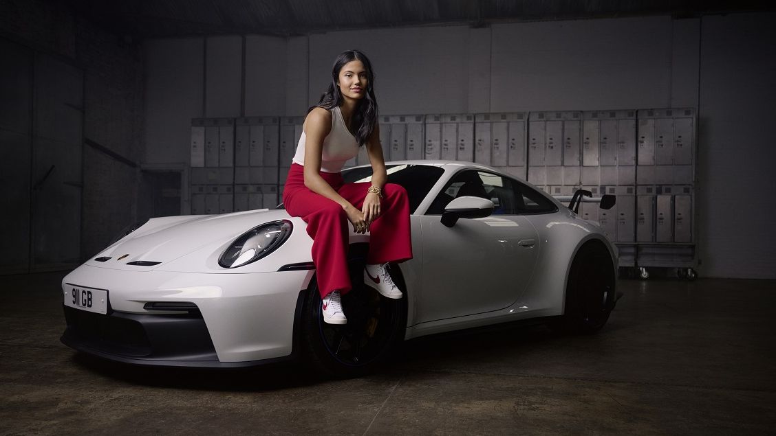 Petenis Inggris, Emma Raducanu, berpose di atas mobil Porsche 911 berwarna putih.