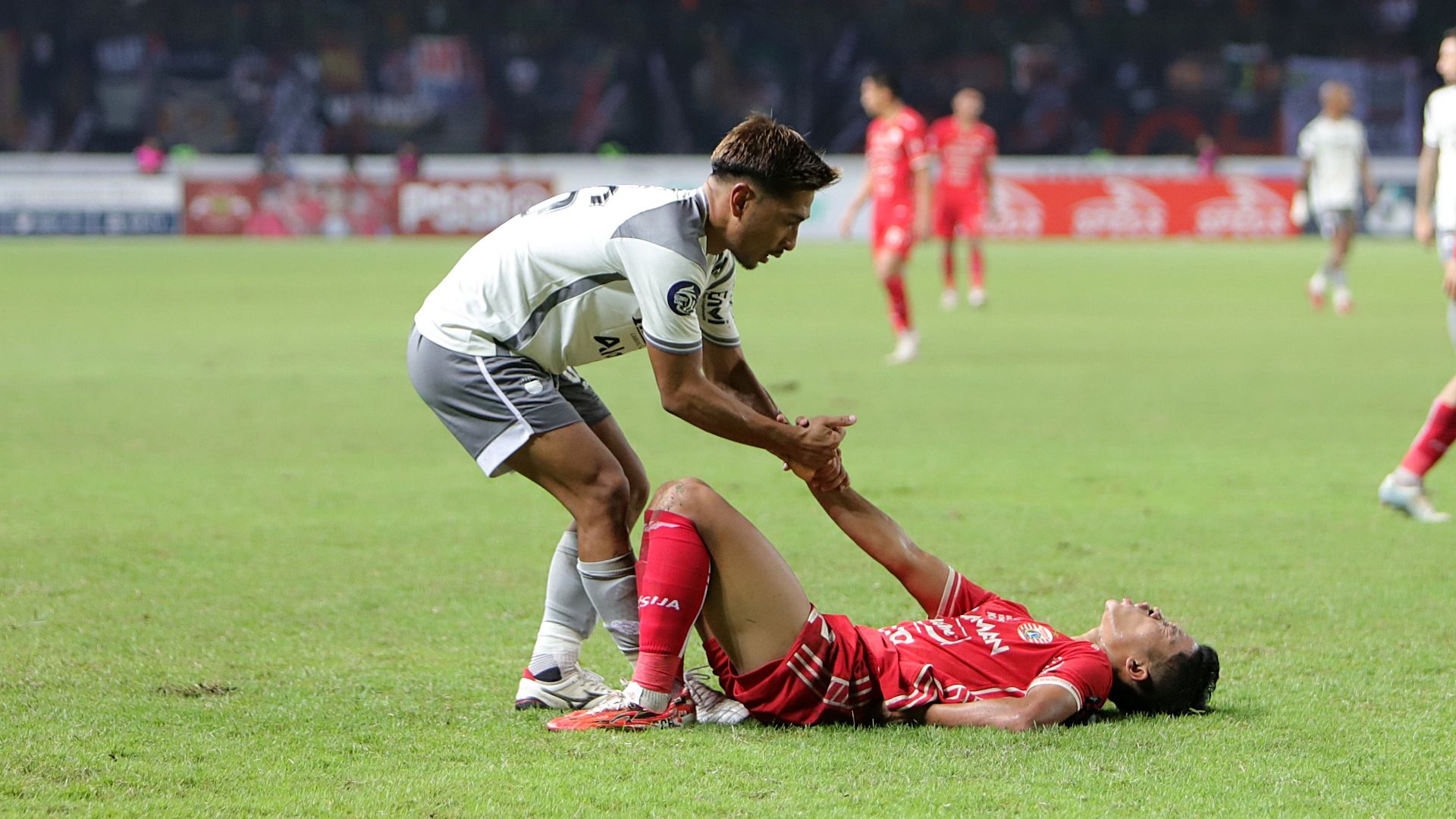 Bek sayap Persib, Daisuke Sato (putih), menolong pemain Persija yang terbaring kesakitan pada laga tunda pekan ke-28 Liga 1 2022-2023 di Stadion Patriot Candrabagha, 31 Maret 2023. (Mario Sonatha untuk Skor.id)